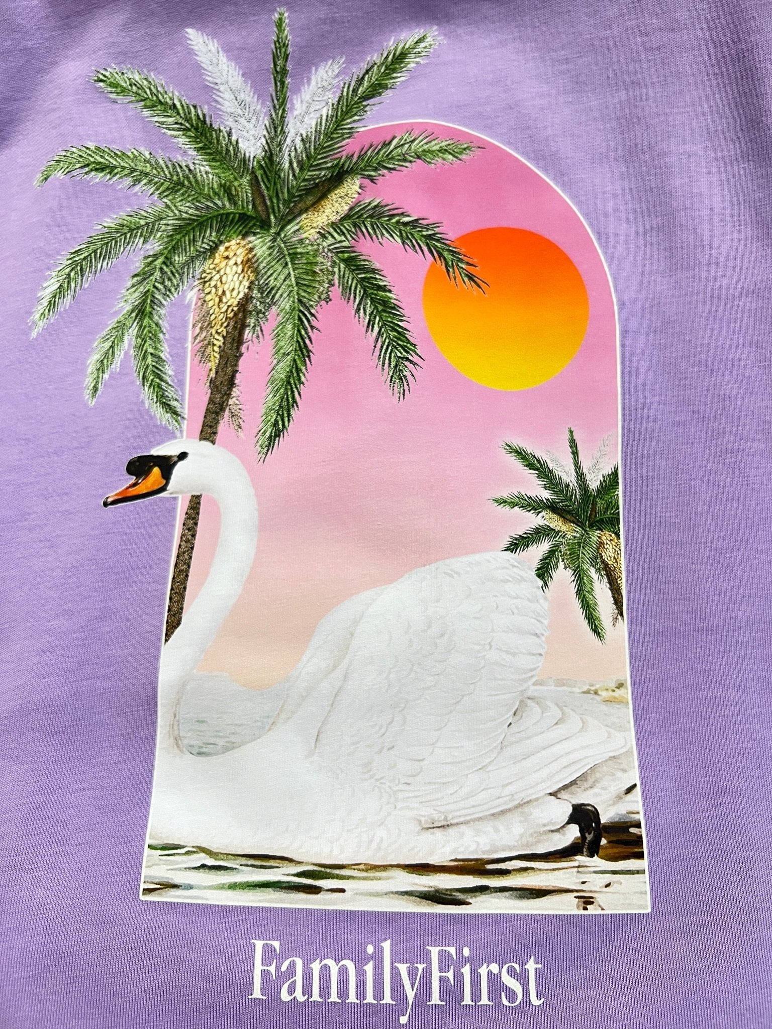 This digital print on the Family First TS2407 T-Shirt Swan Violet by FAMILY FIRST captures the essence of Italian elegance with an illustration of a swan on water, two palm trees, and a sunset in the background. The text "Family First" is featured below, reminiscent of premium cotton's smooth finish.