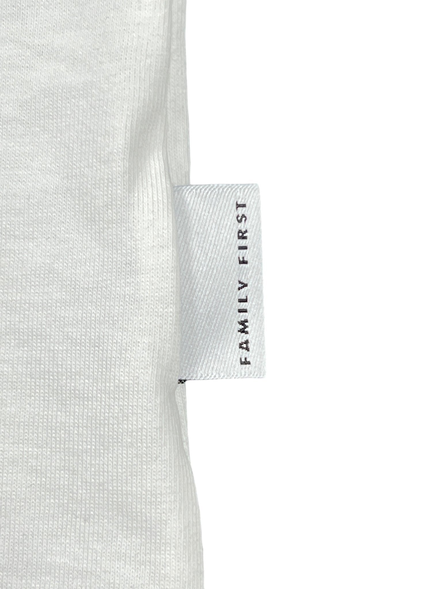 A white fabric label with "FAMILY FIRST" is skillfully sewn into the seam of a gray Family First TS2504 T-shirt Heart Tone White, adding authenticity.