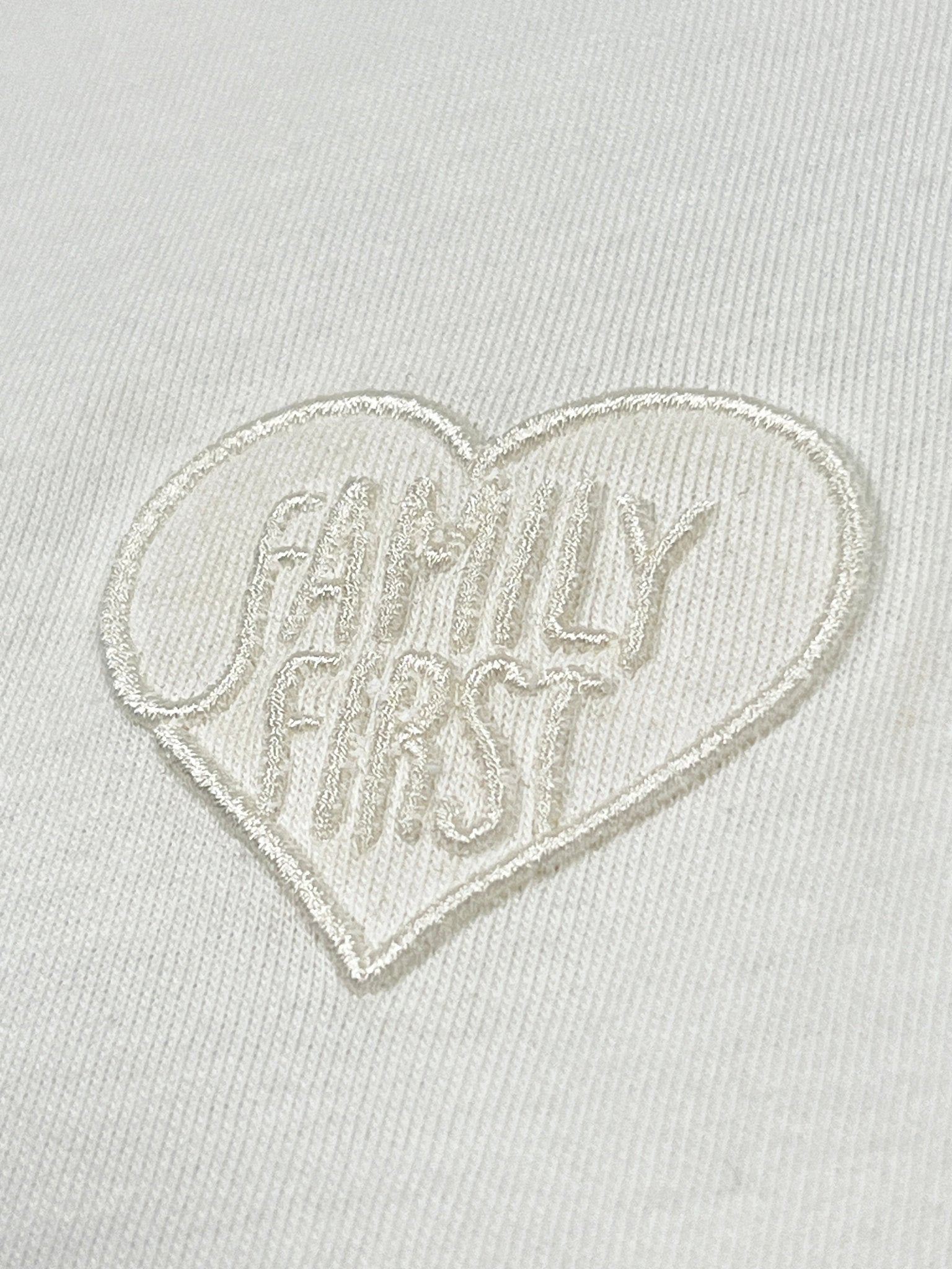 The Family First TS2504 T-shirt by FAMILY FIRST features heart tone white fabric with an embroidered heart and "FAMILY FIRST" in raised white stitching, offering subtle elegance.