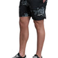 A person wearing FILLING PIECES Chrome Swimshorts Black, a black shirt, and black-and-white sneakers stands with one hand in their pocket.