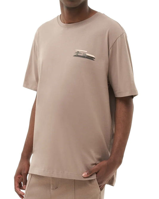 A person wearing the FILLING PIECES CONSTRUCT FOSSIL T-SHIRT, a beige short-sleeve tee made from organic cotton and featuring a small abstract logo on the chest, paired with matching beige pants.