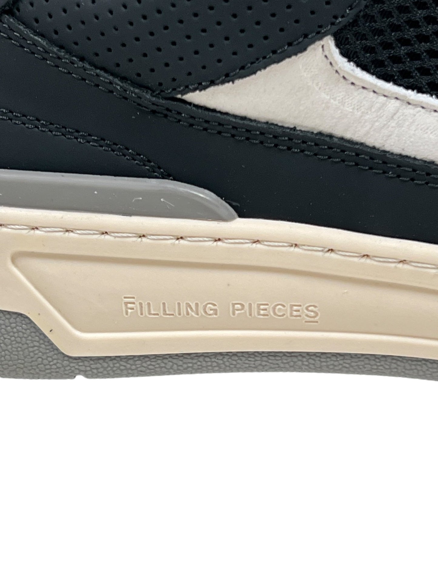 Close-up of the side of a FILLING PIECES CRUISER BLACK shoe, featuring a black and white upper crafted from premium organic Nappa leather, with a beige-colored sole and the brand name "Filling Pieces" engraved on the midsole.