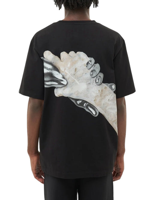 A person wearing the FILLING PIECES HANDSHAKE ELEMENTS BLK T-SHIRT from FILLING PIECES, made of 100% organic cotton, featuring an image of two clasping hands on the back, viewed from behind.