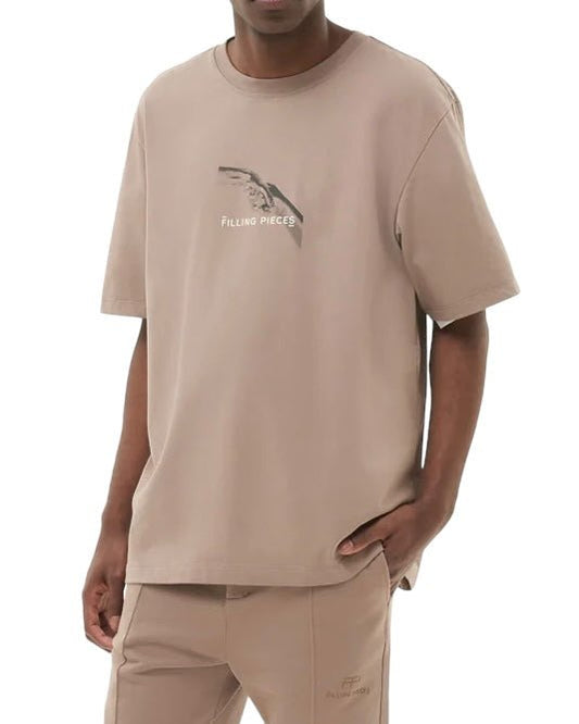 Person wearing a "FILLING PIECES HANDSHAKE FOSSIL T-SHIRT" with the FP handshake backprint, paired with matching beige pants, stands against a white background.