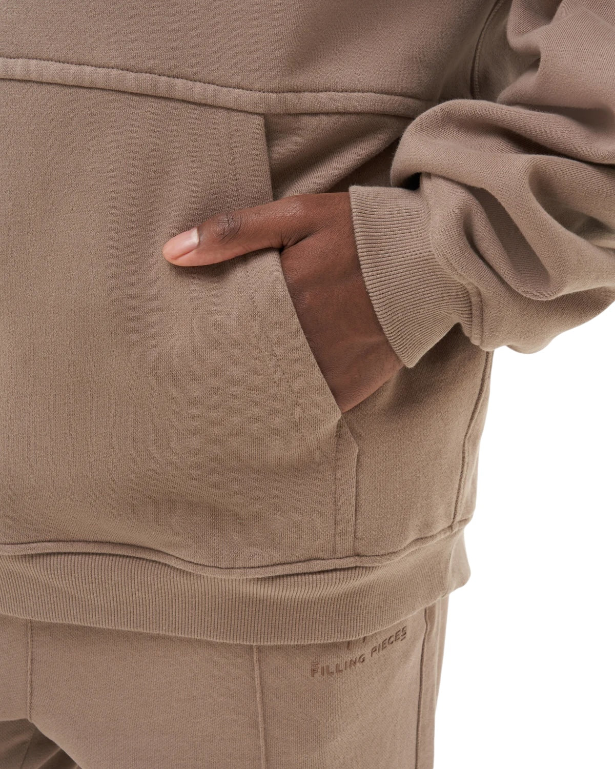 Wearing the Filling Pieces Hoodie Pavilion Fossil by FILLING PIECES, paired with matching pants, a person displays understated elegance with a hand in their pocket.