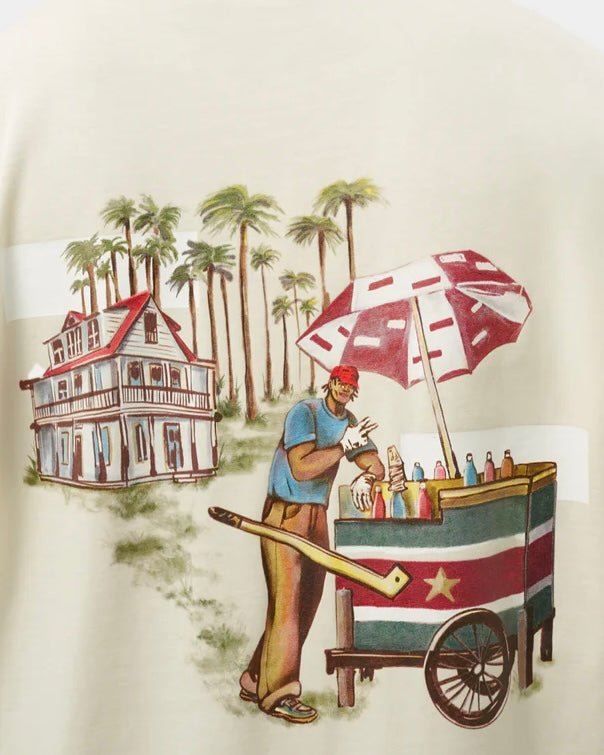 Illustration on a Filling Pieces t-shirt featuring a tropical scene with a man pushing a cart of colorful bottled drinks under an umbrella, near a large house surrounded by palm trees. This graphic jersey is made from organic cotton.