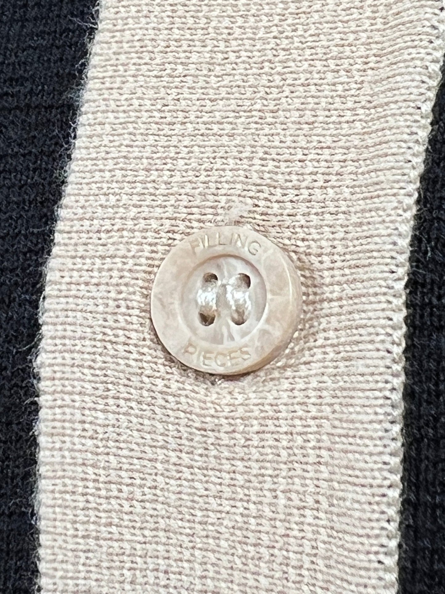 Close-up of a beige "Filling Pieces" branded button on the FILLING PIECES KNIT POLO BLACK fabric featuring black and beige stripes.