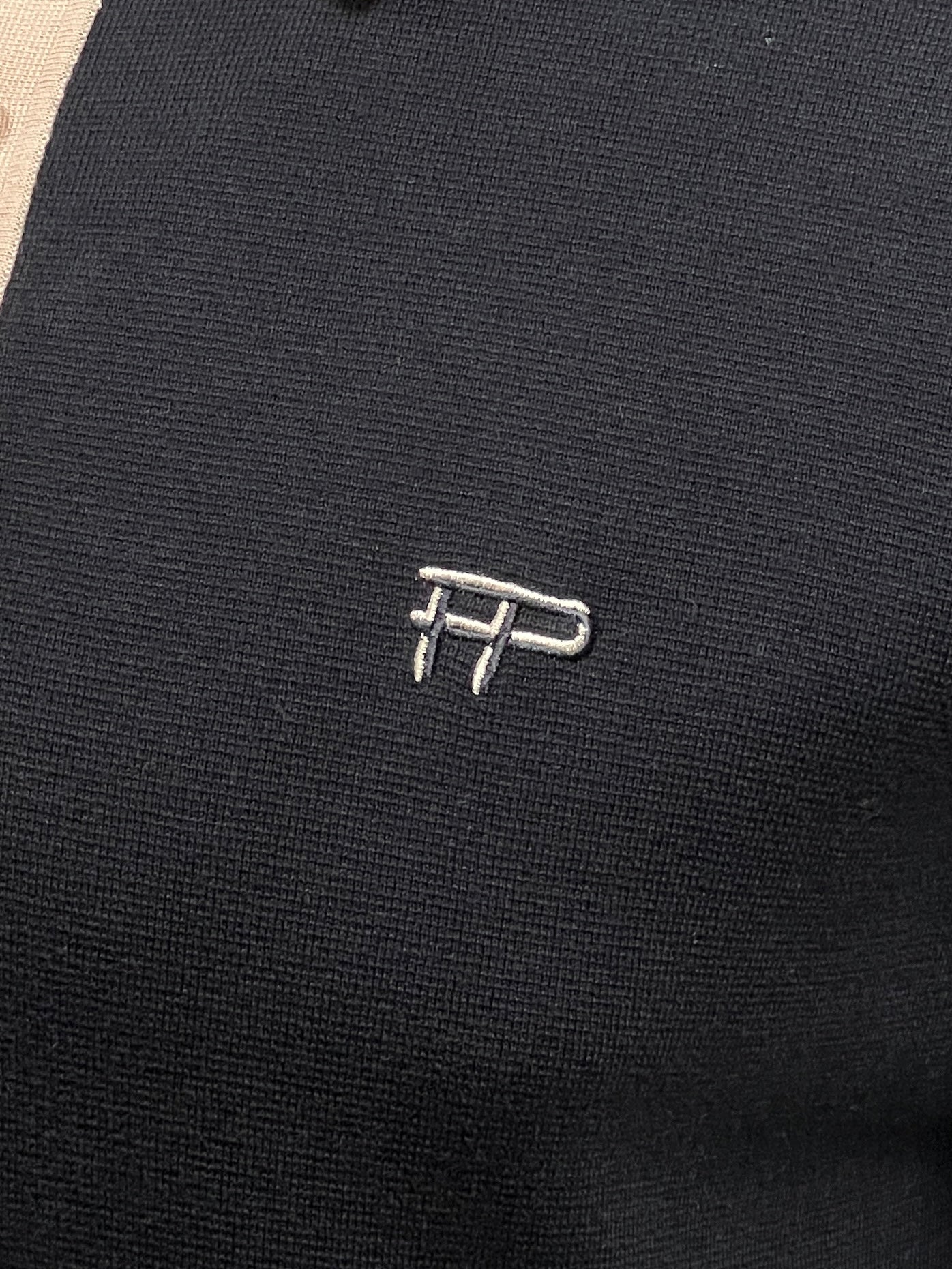 Close-up of the dark fabric from the FILLING PIECES KNIT POLO BLACK, showcasing a small, embroidered design with the letters "IP" in a light thread, complemented by buttons branded with FILLING PIECES.