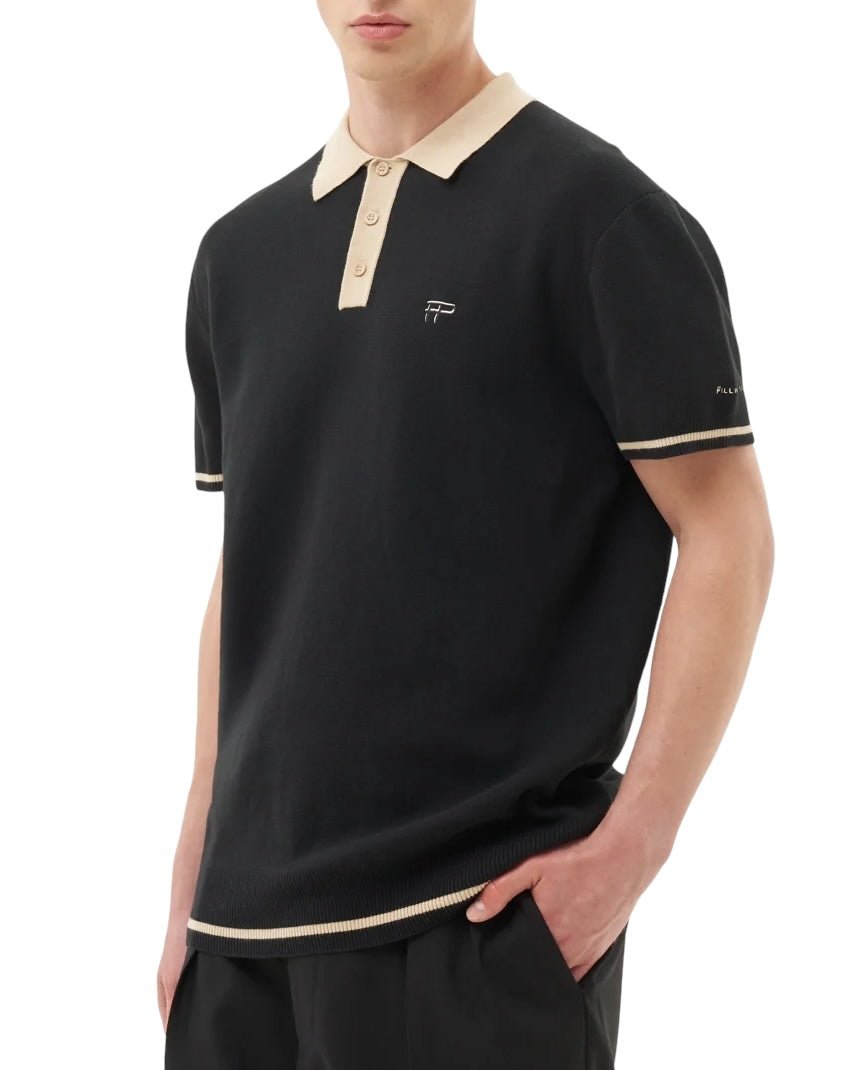 A person is wearing the FILLING PIECES KNIT POLO BLACK shirt, crafted from 100% cotton. The shirt features a beige collar and sleeve trim, FP branded buttons, and a small embroidered logo on the chest.