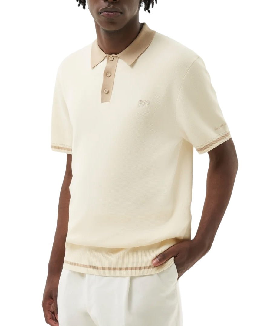 A person is dressed in the FILLING PIECES KNIT POLO RICE BROWN made from 100% cotton, featuring tan collar and sleeve accents and FP branded buttons, standing with one hand in their pocket.