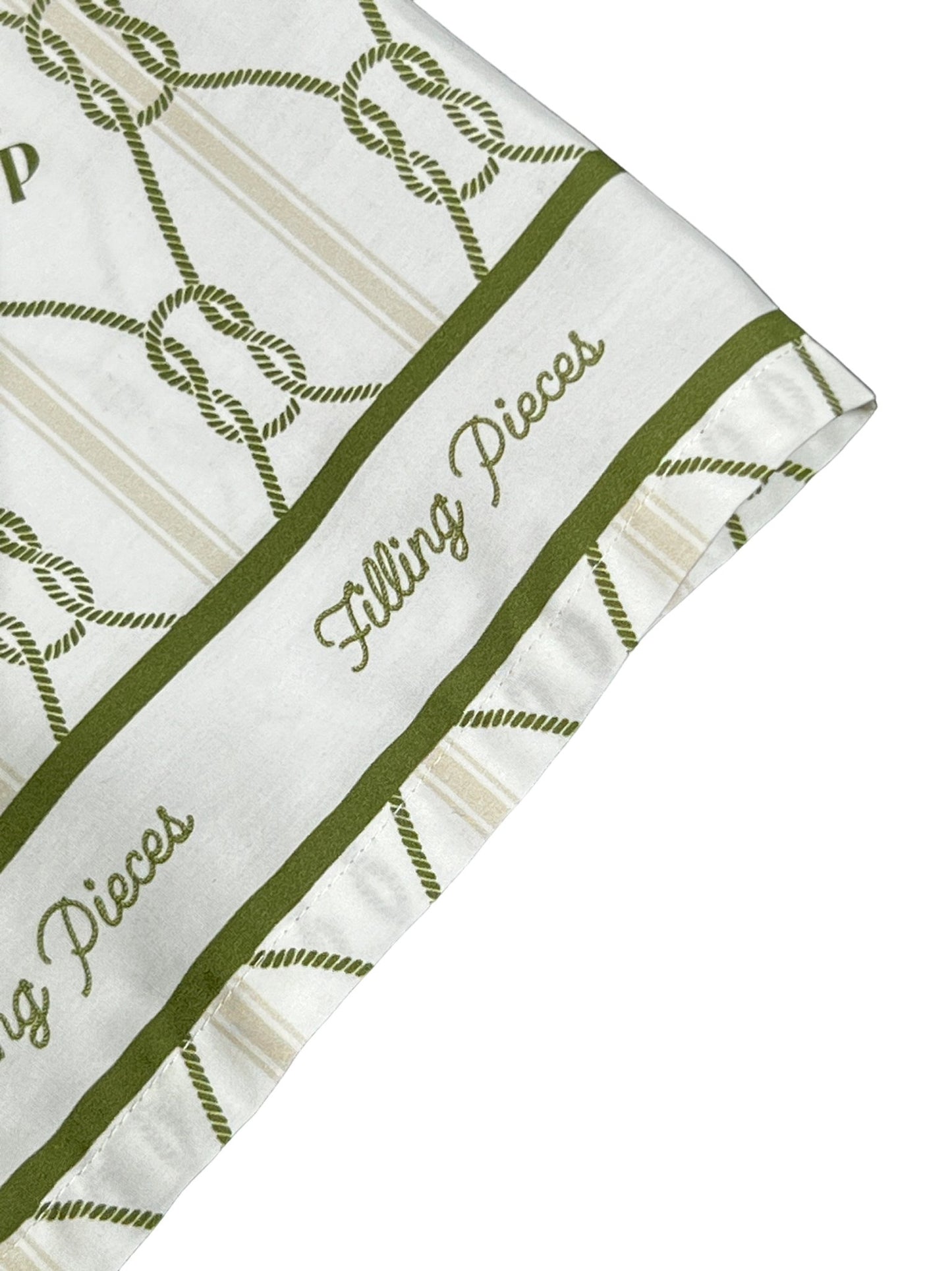 A close-up of a white FILLING PIECES RESORT MONOGRAM SHIRT MILK with printed text "FILLING PIECES" and green decorative patterns on the edges.