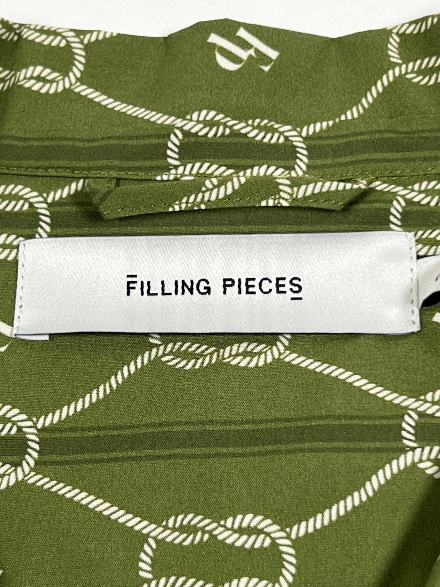 The Filling Pieces Resort Monogram Shirt Olive is made from 100% organic cotton, featuring an olive green fabric with an all-over rope pattern and a white label displaying "FILLING PIECES" in black text.