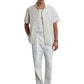 A man wears the Filling Pieces Resort Shirt Petal by FILLING PIECES, a cream linen-viscose blend shirt, paired with a white undershirt, white trousers, black belt, and patterned black loafers.