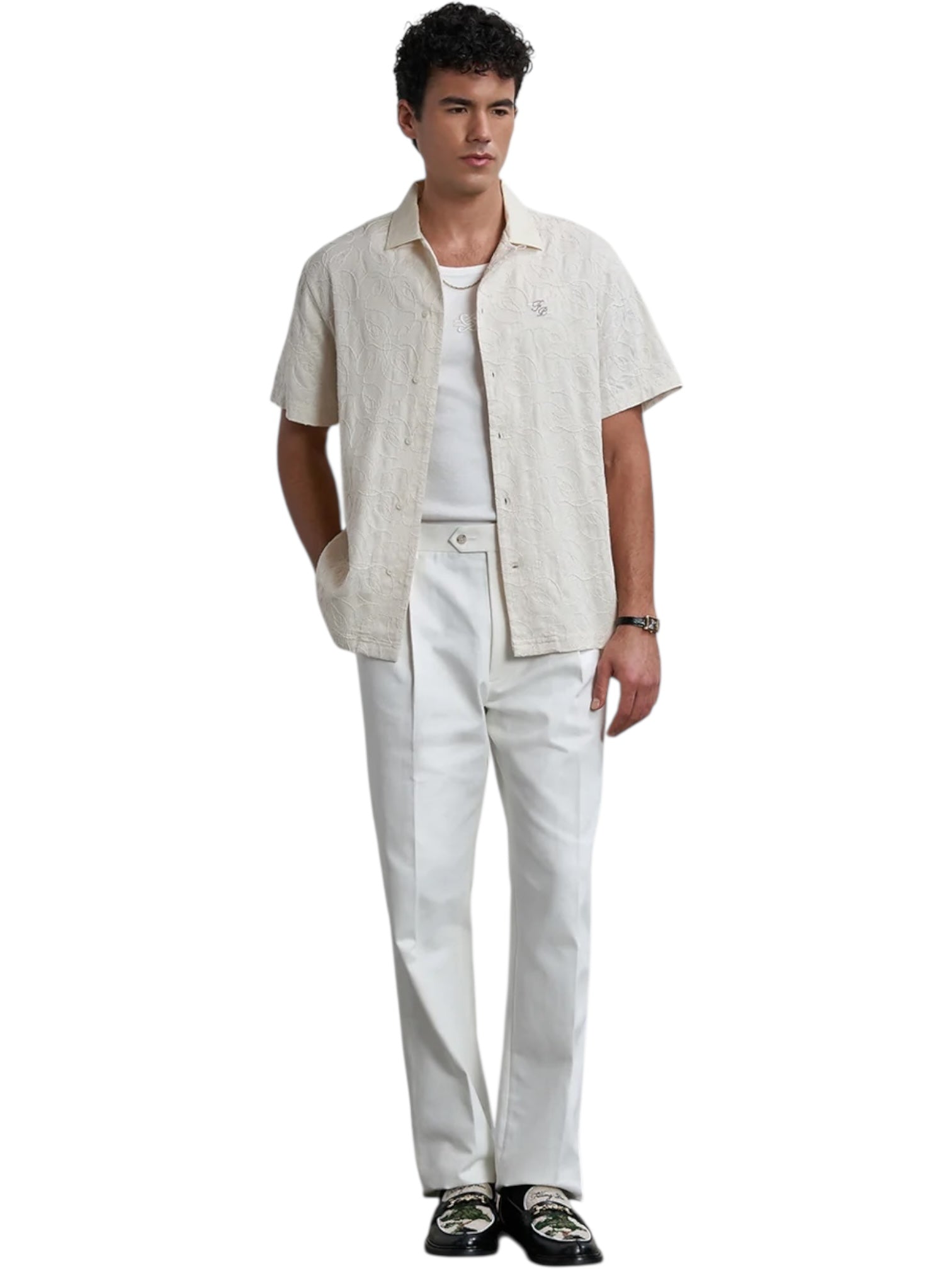 A man wears the Filling Pieces Resort Shirt Petal by FILLING PIECES, a cream linen-viscose blend shirt, paired with a white undershirt, white trousers, black belt, and patterned black loafers.