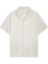 The Filling Pieces Resort Shirt Petal by FILLING PIECES is a short-sleeved, off-white linen-viscose blend shirt with a subtle texture, notched collar, and small floral embroidery logo on the left chest.