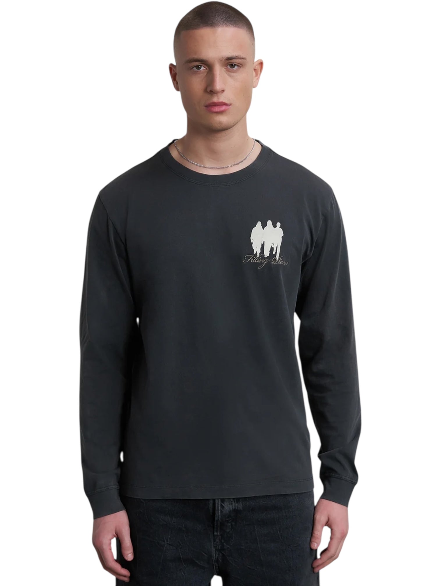 A person wears the FILLING PIECES United By Generations L/S Vintage Black shirt, a dark organic cotton top with premium softness and a small “United by Generations” graphic on the chest, standing against a plain white background.