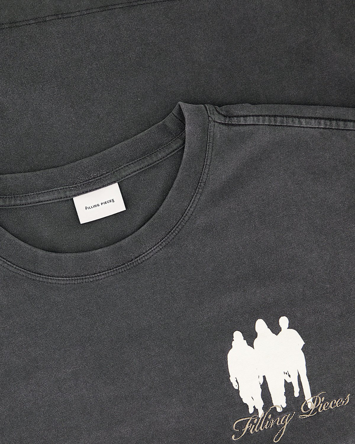 Close-up of the Filling Pieces United By Generations L/S Vintage Black t-shirt by FILLING PIECES, crafted from soft organic cotton, featuring a white graphic of three figures and the brand’s name on the front.