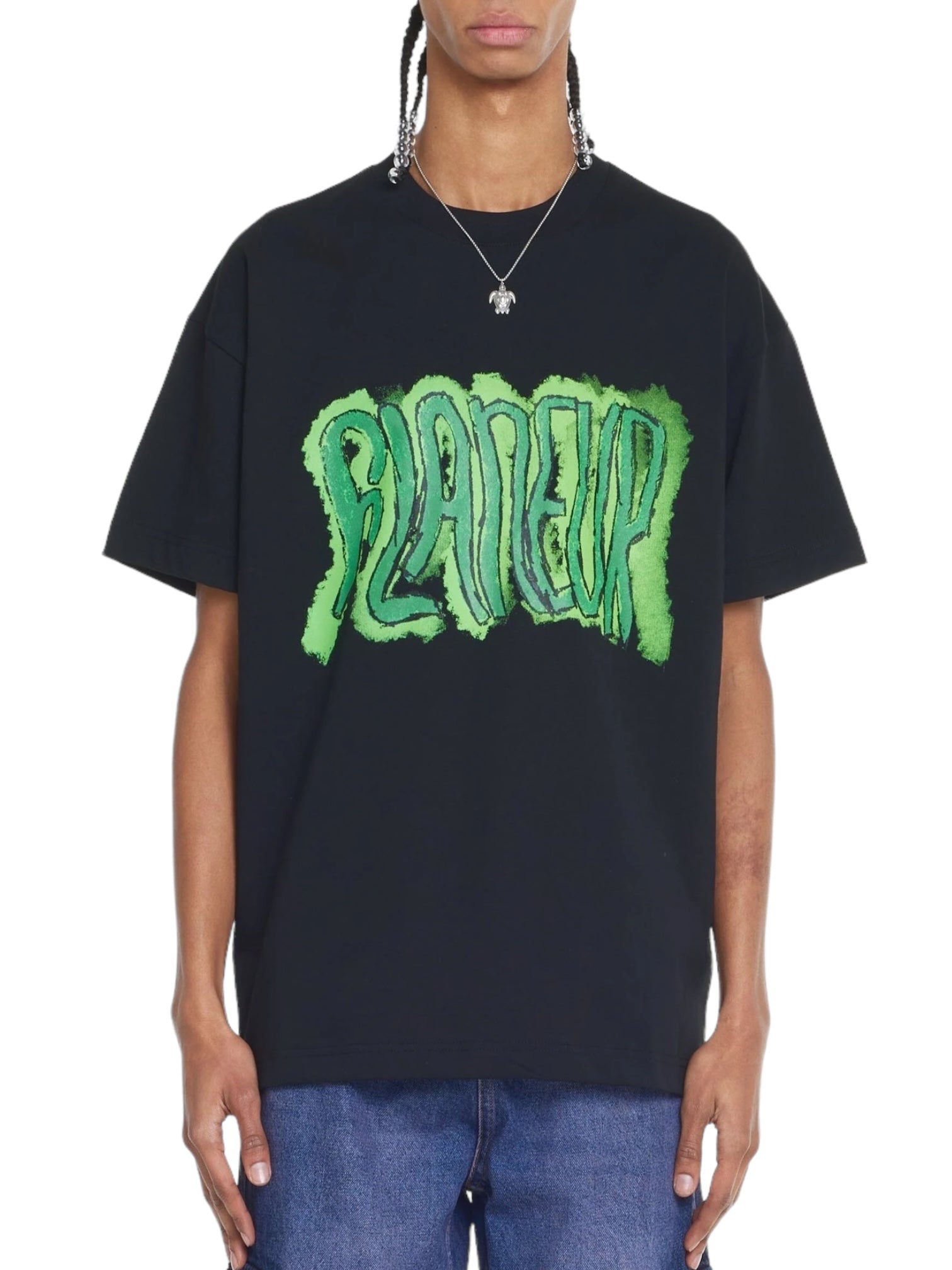 A flâneur in the Flaneur Artist T-Shirt Black by FLANEUR, made from cotton jersey with green graffiti-style text, completes their look with a necklace and blue jeans as they saunter effortlessly.