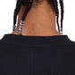 A close-up shows the back of a person's head wearing the FLANEUR Artist T-Shirt Black, a black cotton jersey with beaded braids and "FLÂNEUR" elegantly embroidered.