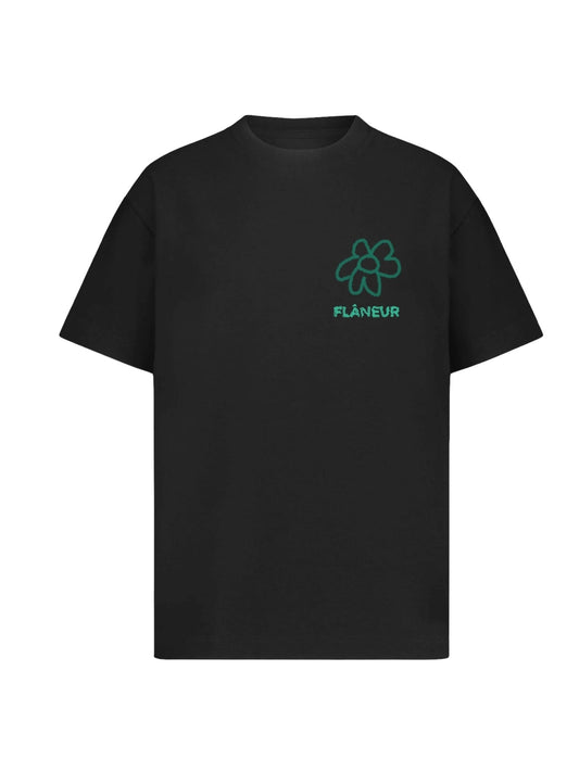 The FLANEUR black T-shirt features the word "FLÂNEUR" in graphic lettering along with a green flower doodle graphic on the upper left chest area.