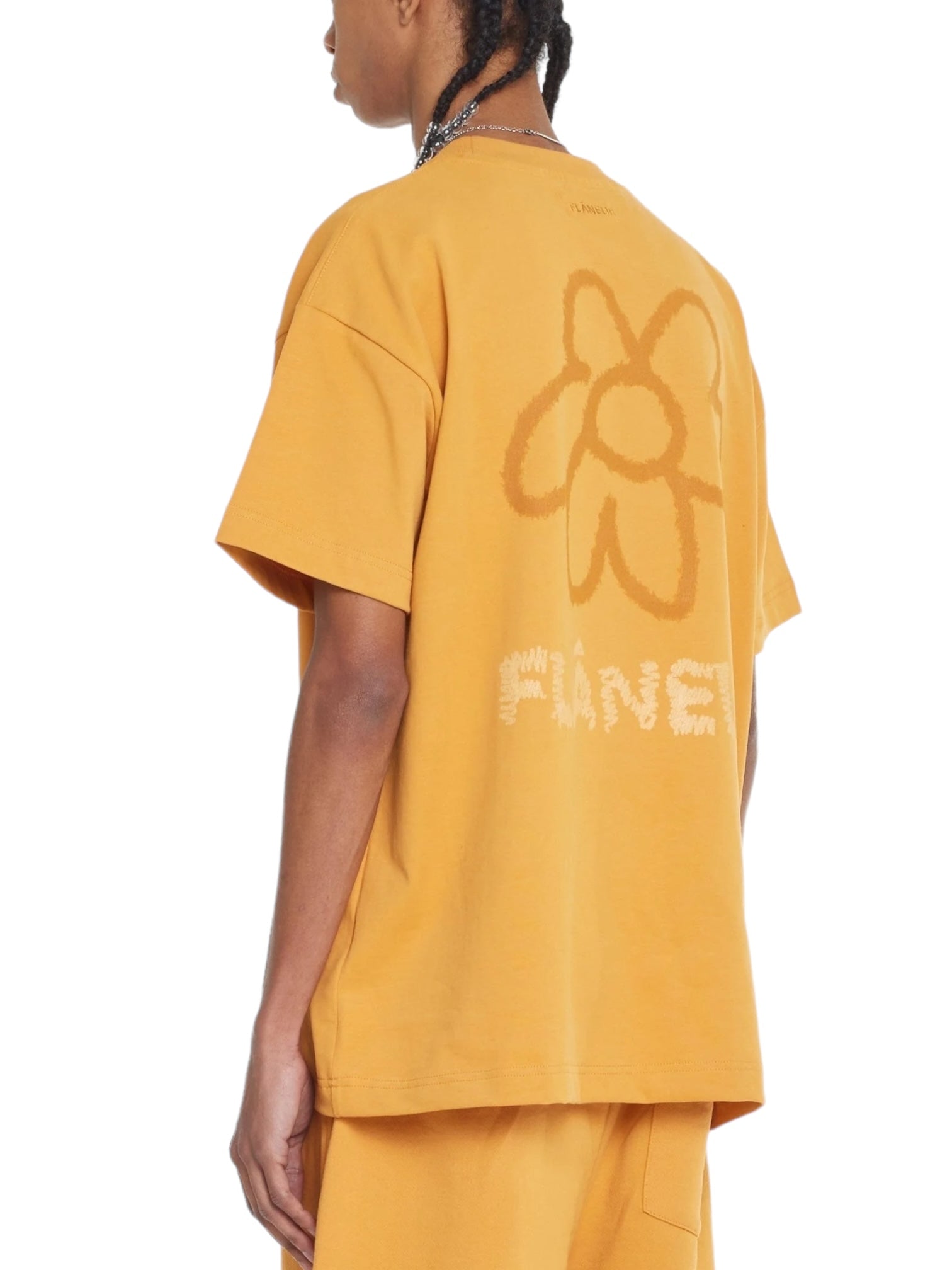 Person wearing an oversized mustard-colored "Flaneur Flower Doodle T-Shirt Org" by FLANEUR, featuring a flower doodle graphic and the word "FUNE" on the back.