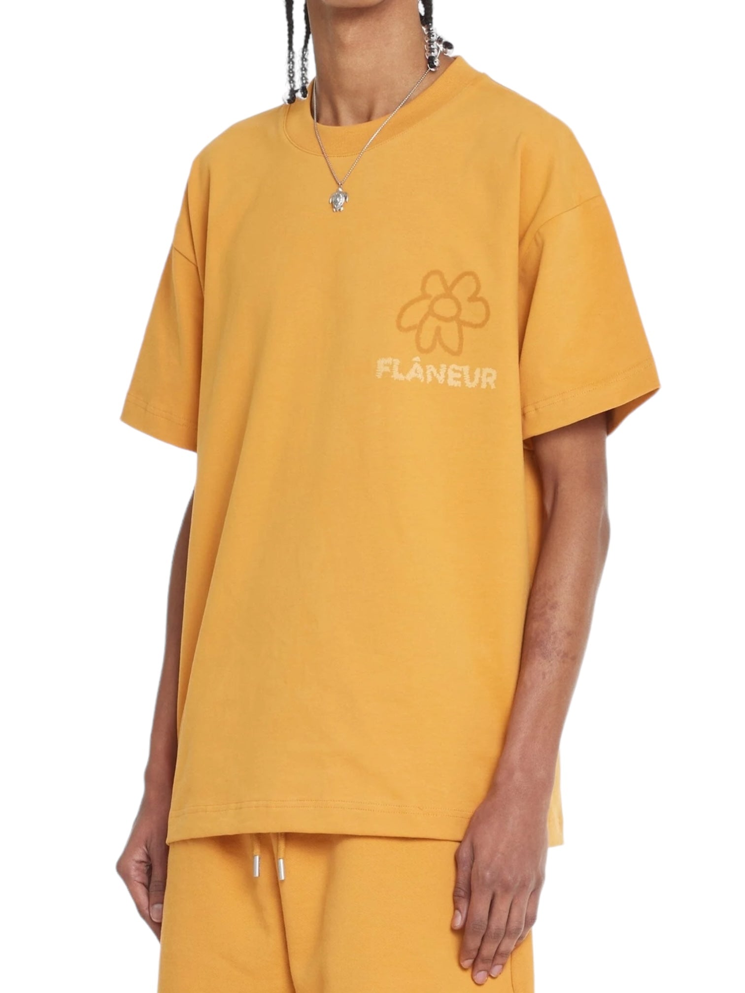 Someone shows off the Flaneur Flower Doodle T-Shirt Org by FLANEUR, a mustard yellow cotton jersey boasting the "FLÂNEUR" text and an adorable flower doodle graphic, perfectly paired with matching pants.