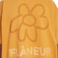A person wearing the Flaneur Flower Doodle T-Shirt Org in yellow, featuring a large flower doodle graphic and the brand name "FLANEUR" on the back.