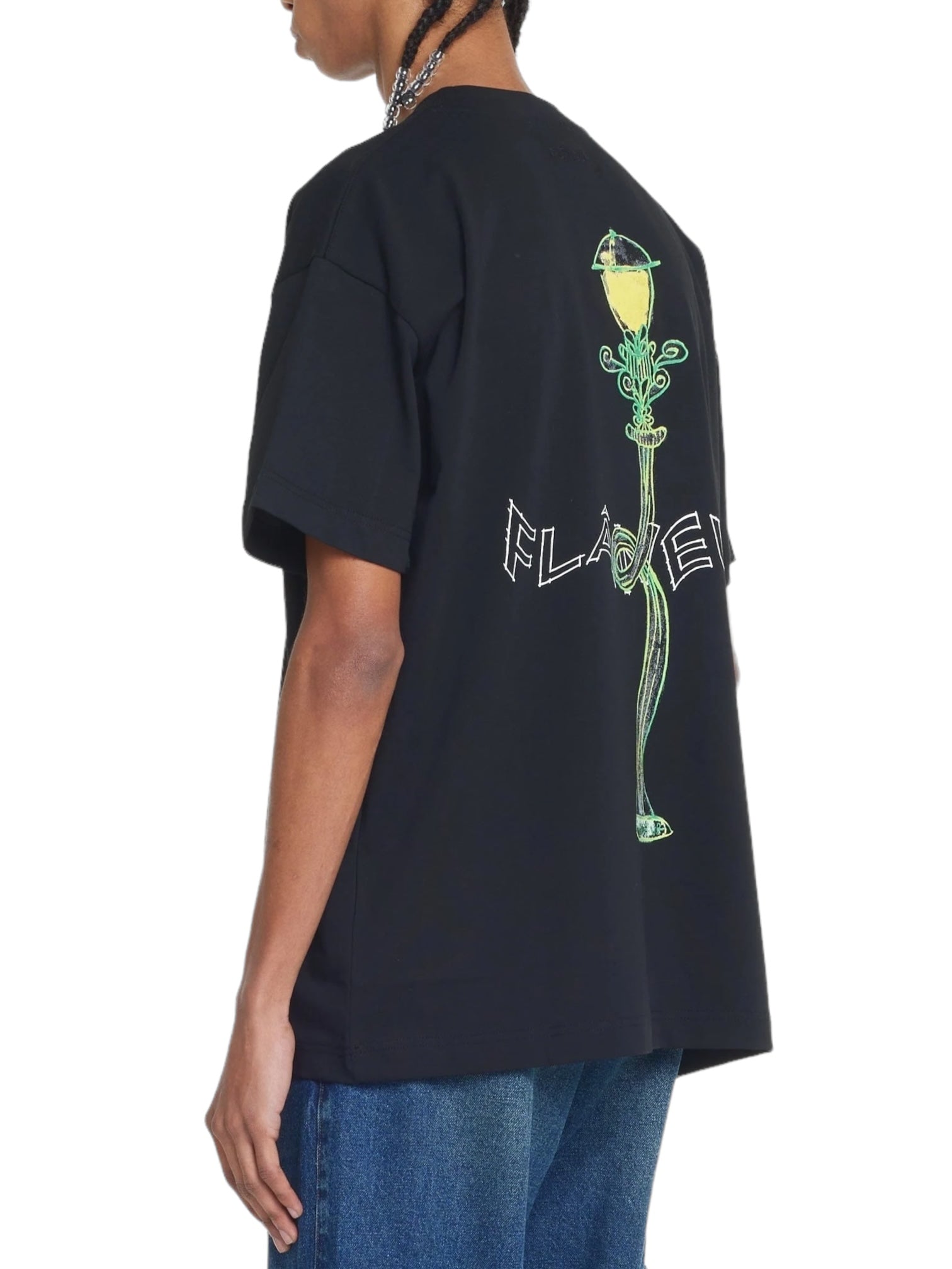 The person is wearing a Flaneur Lantern T-Shirt in black by FLANEUR, which has a striking green illustration and the word "FLAKE" on the back, perfectly paired with blue jeans.