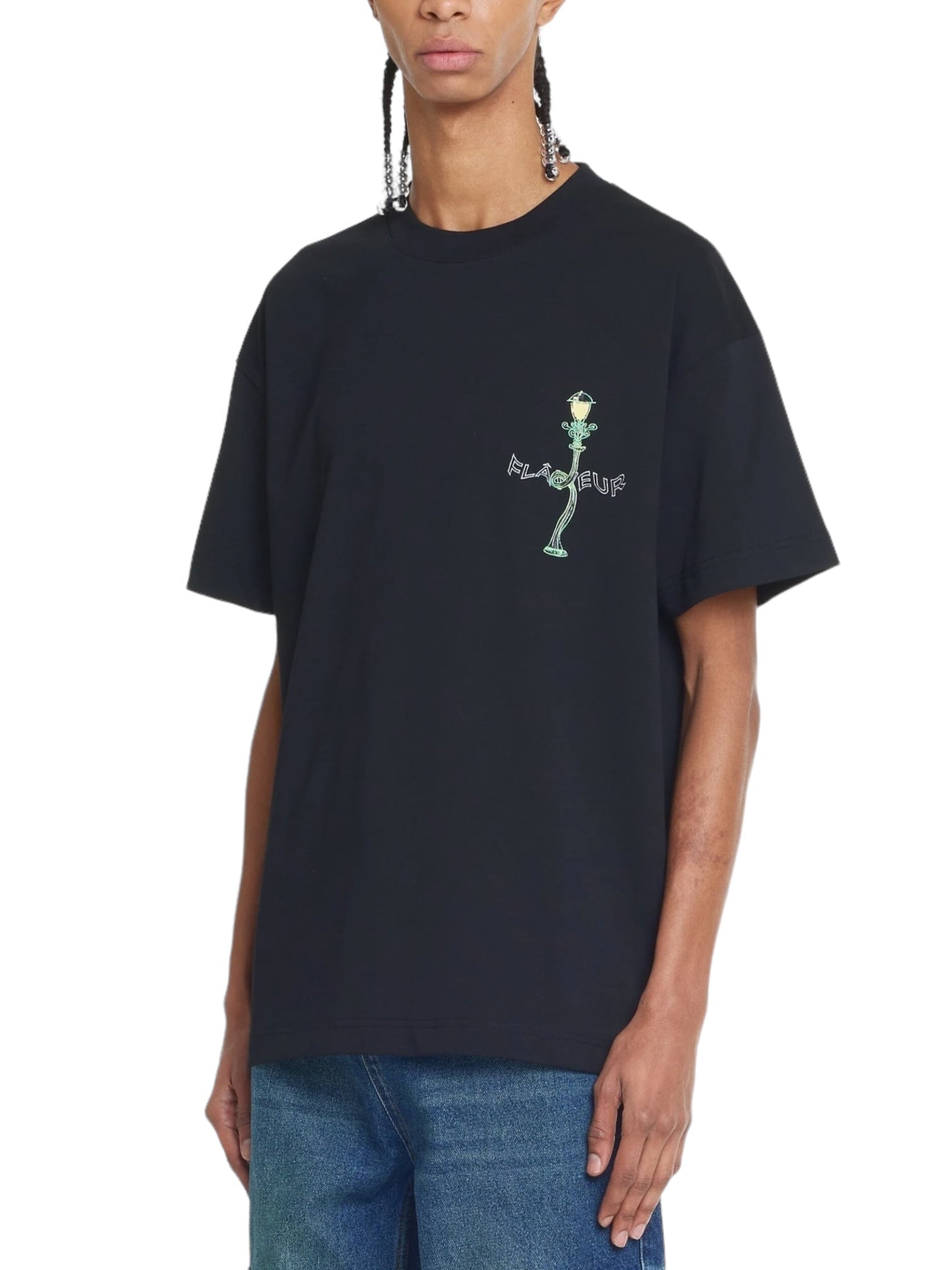A person wearing a black FLANEUR Lantern T-Shirt featuring a small Flâneur graphic on the front, paired with blue jeans.