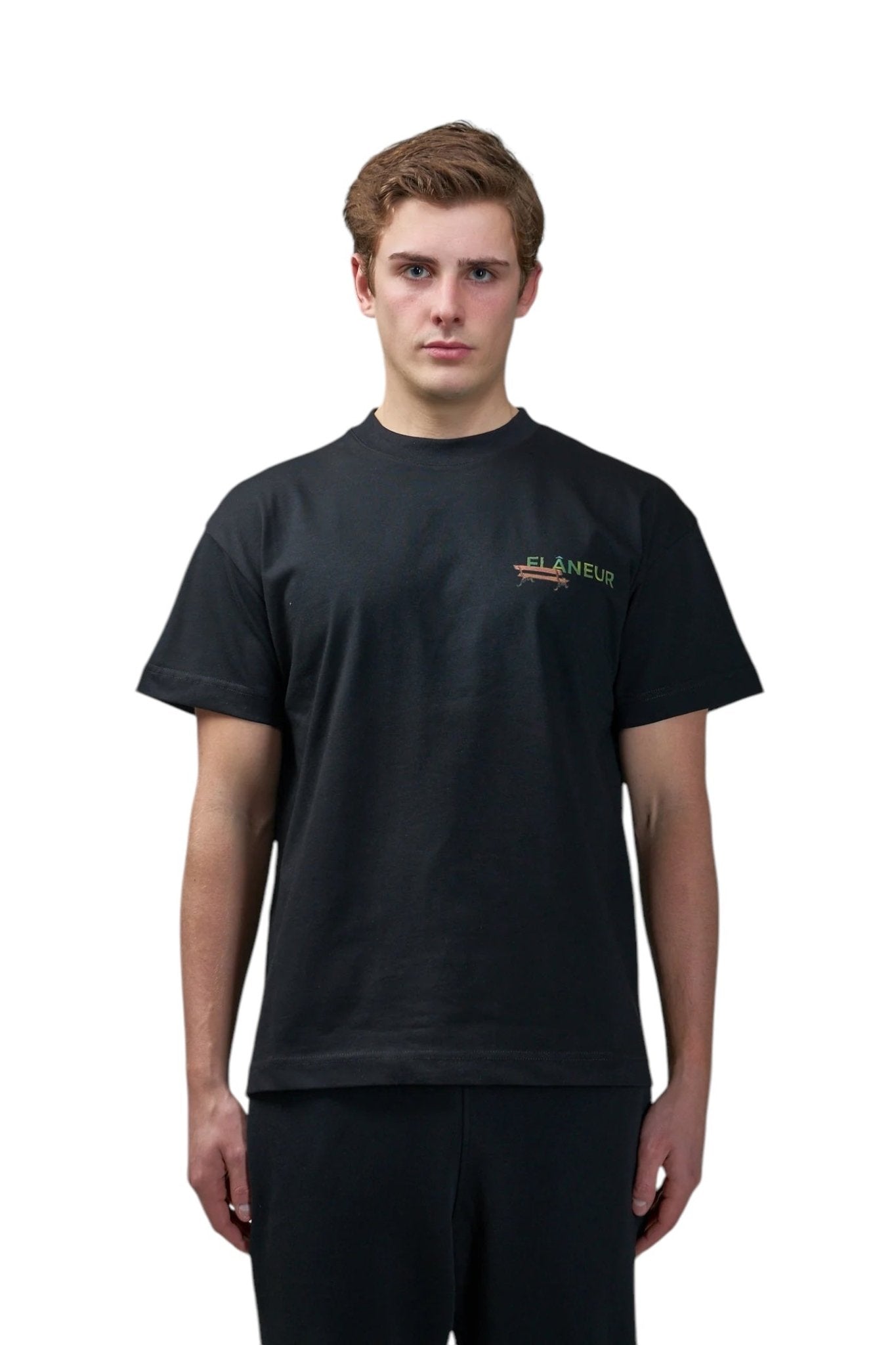 A person faces forward wearing the FLANEUR Lanterns of Love T-Shirt Black, featuring a minimalist design with the brand’s name in small print on the left chest, embodying the lanterns of love spirit.