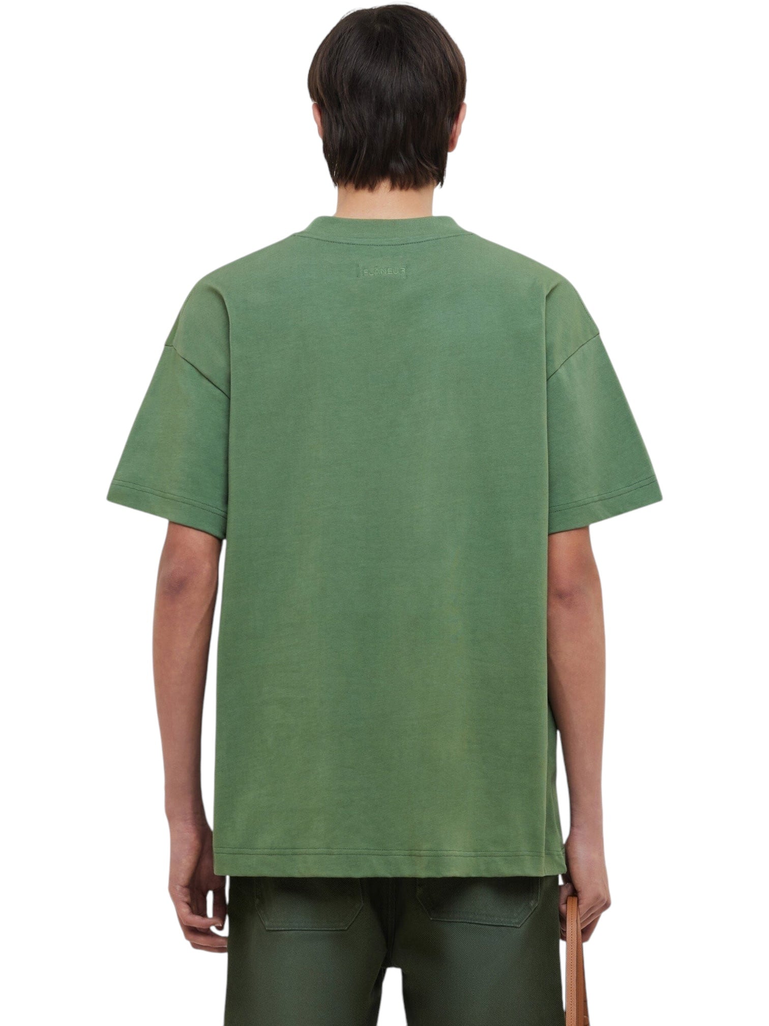 A person is shown from the back against a plain white background, wearing a loose-fitting FLANEUR Flaneur Logo T-Shirt Khaki and dark green pants.