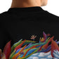 A person shown from behind wearing the FLANEUR Flaneur Passage of Time T-Shirt Black, featuring a colorful abstract plant and cloud design on the back.