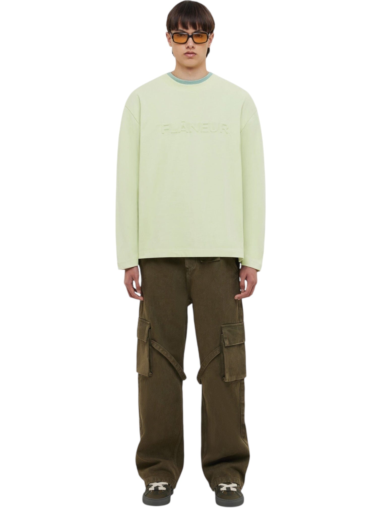 A person wearing a light green long-sleeve shirt with "FLÂNEUR" text, FLANEUR Flaneur Phone Pocket Cargo Trousers in army green, and dark sneakers stands against a white background.
