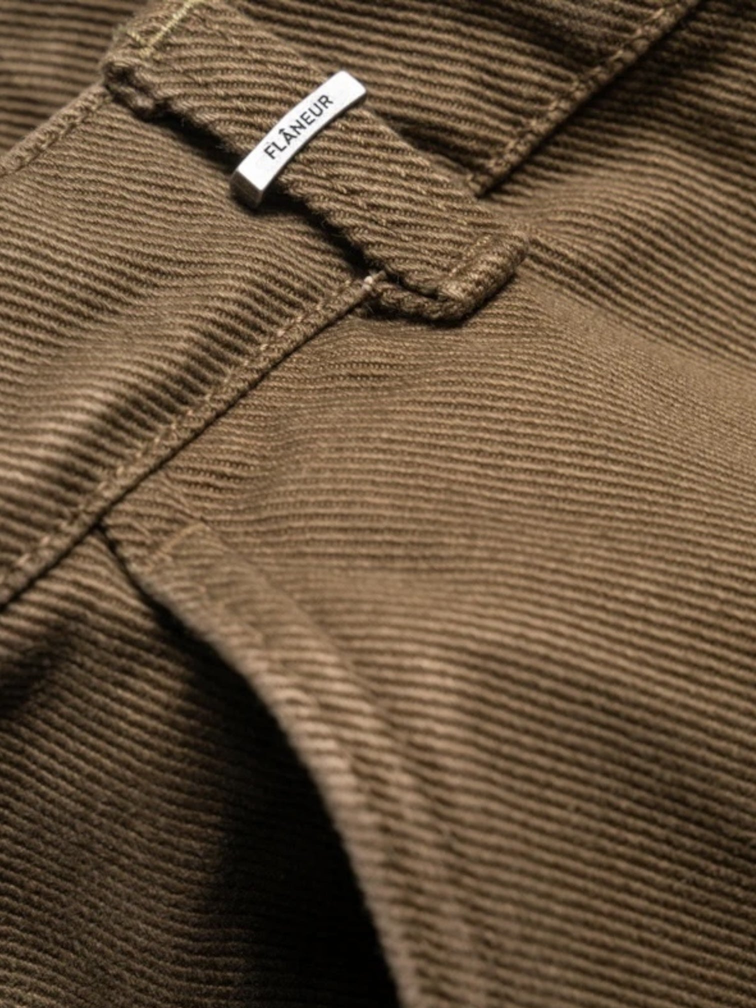 Close-up of army green corduroy fabric featuring a "FLANEUR" label attached to a belt loop, showcasing the cotton texture of the Flaneur Phone Pocket Cargo Trousers.