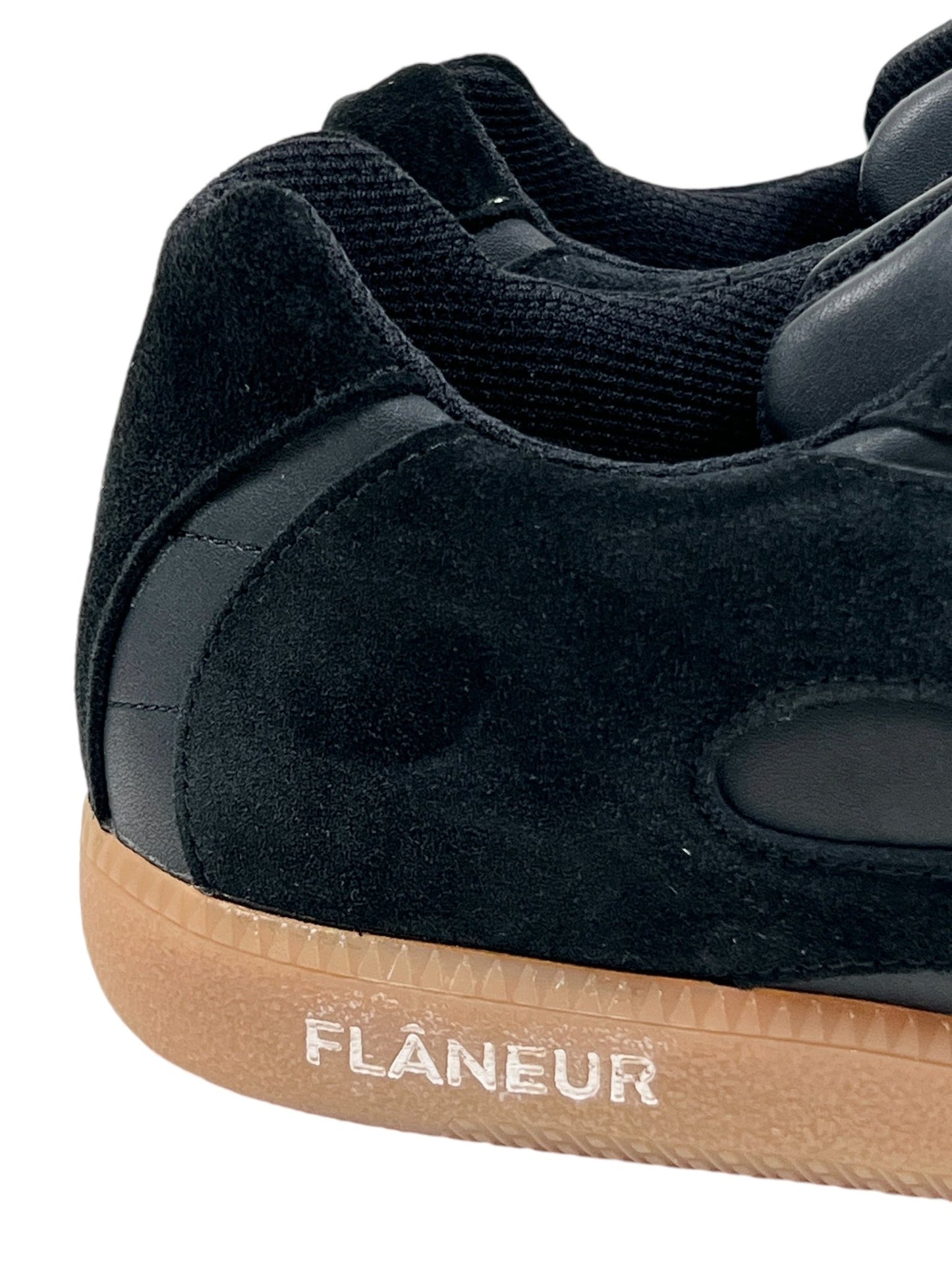 Close-up of the FLANEUR TIVOLI RUNNER BLACK, featuring black suede with matching black laces and a light brown rubber sole. The sneaker prominently displays the white inscription "FLANEUR" near the heel, combining an exquisite blend of style and eco-conscious design through sustainably sourced materials.