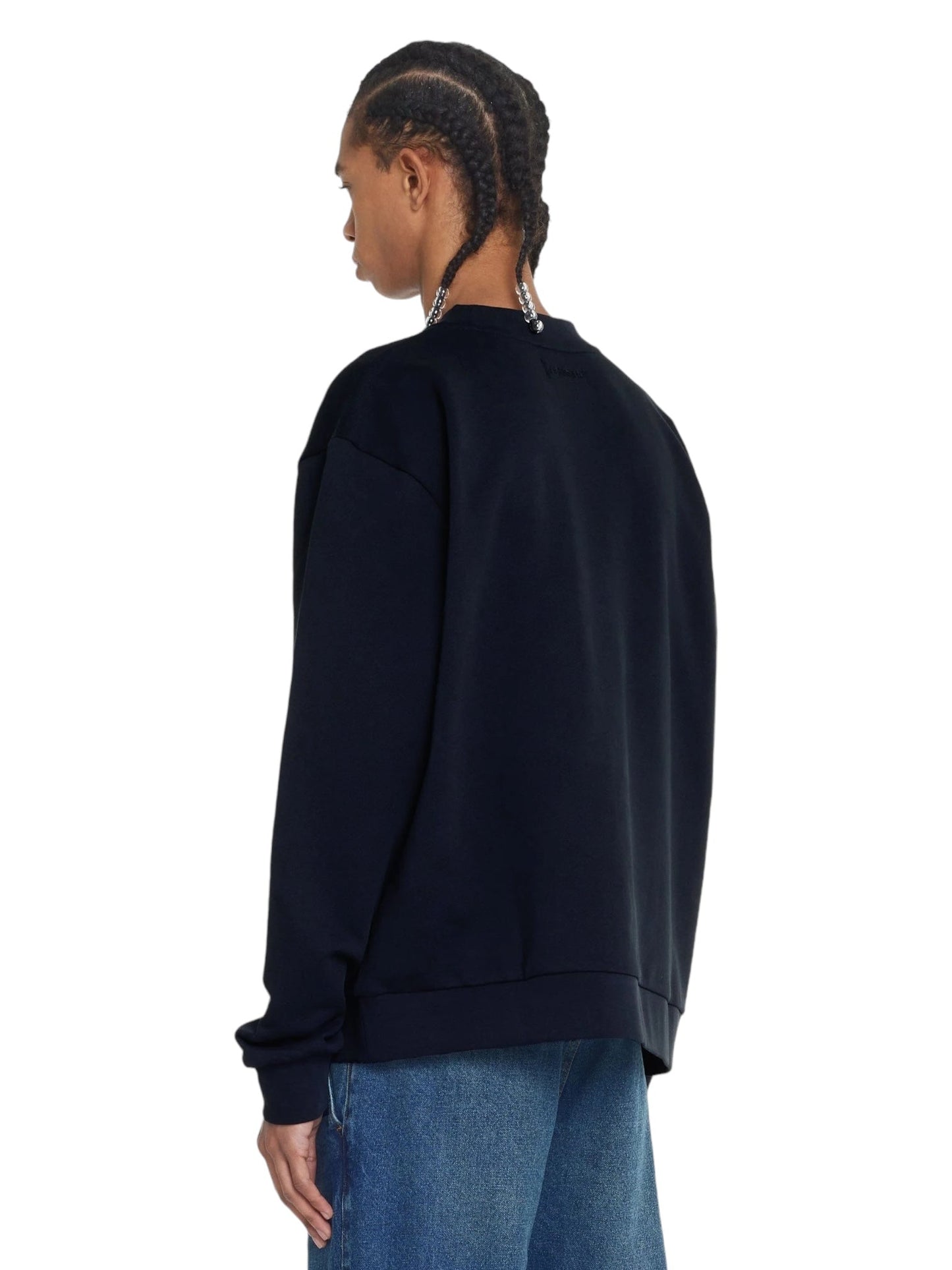 A person with braided hair, wearing the FLANEUR FLOWER STALK SWEATER in black made of soft cotton jersey and blue jeans, is shown from the back.