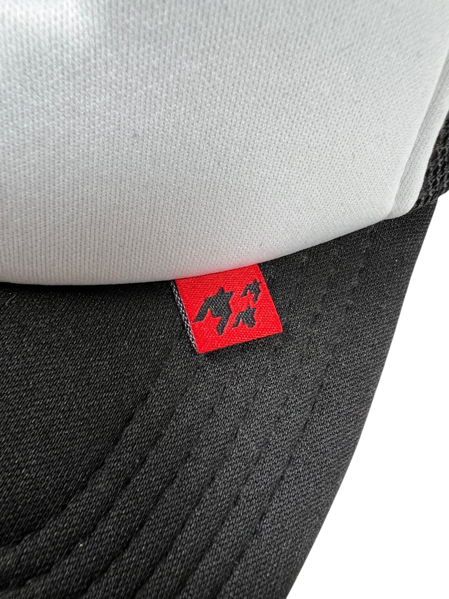 Close-up of the FREE REFILLS Free Refills Harley Trucker (FR-C3-39) hat in white/black, featuring a small red tag with black graphic symbols.