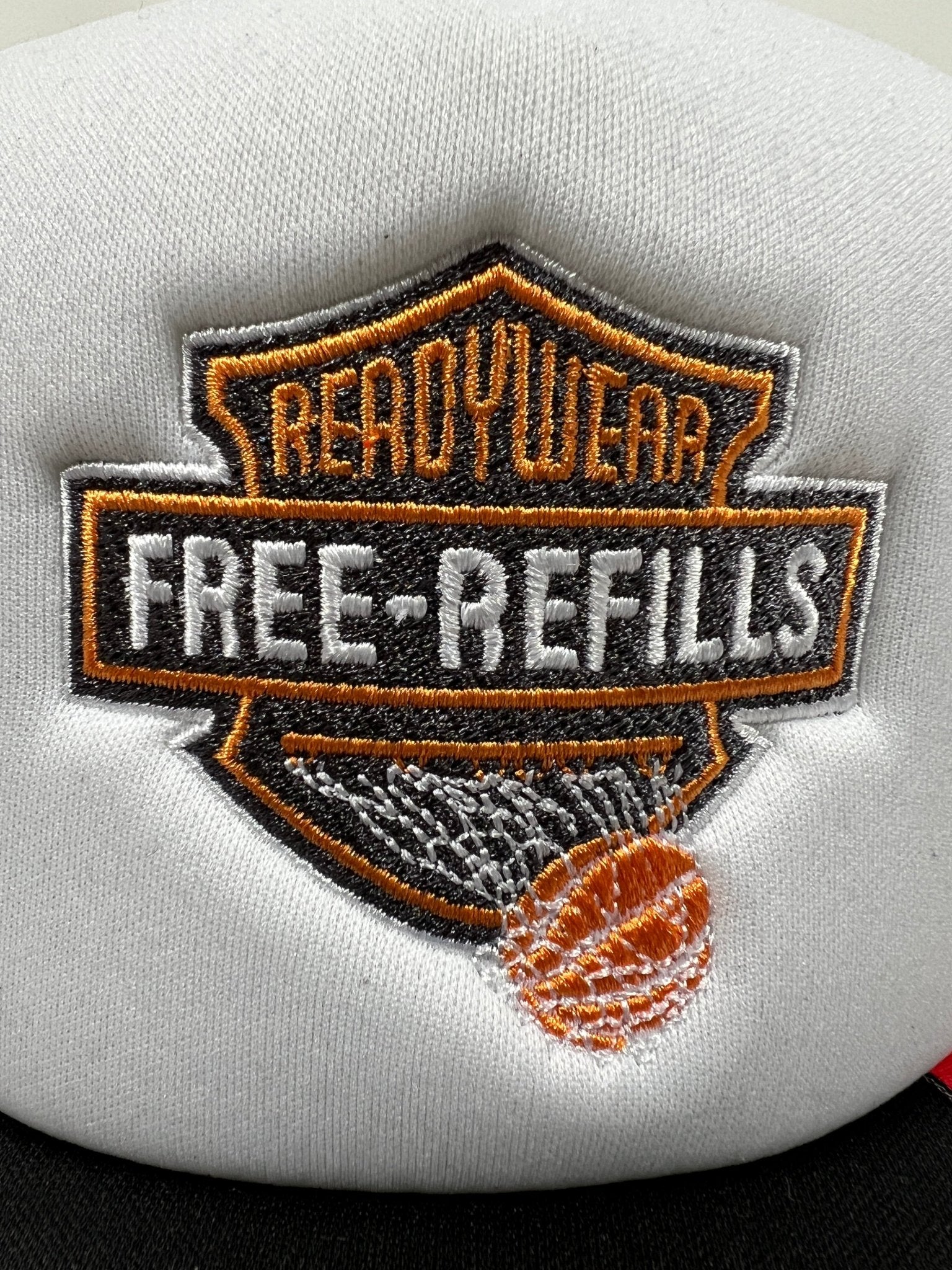 A close-up of the FREE REFILLS Free Refills Harley Trucker (FR-C3-39) in White/Black, featuring a white fabric patch with "READYWEAR FREE-REFILLS" in orange and white text and an orange basketball, echoing classic trucker hat style.