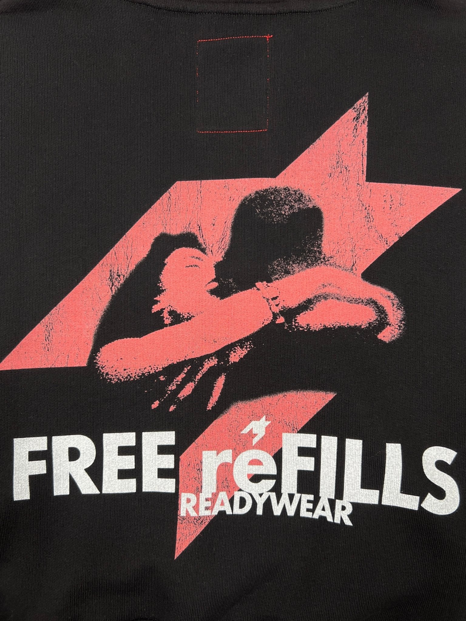 The FREE REFILLS Free Refills Romance Tee (FR-C3-12) features a graphic of two people embracing before a pink lightning bolt and "FREE reFILLS READYWEAR" text, on vintage black heavyweight cotton with a faded wash for lasting comfort and style.