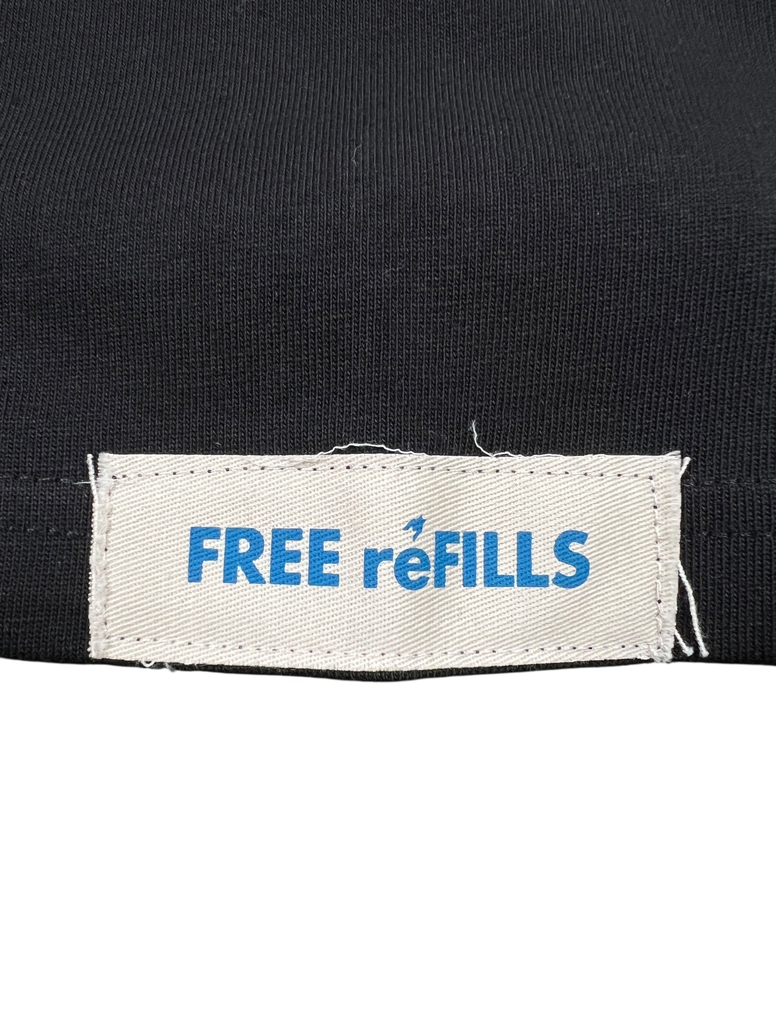 The FREE REFILLS Free Refills Romance Tee (FR-C3-12) in vintage black features a white fabric label with blue "FREE reFILLS" text sewn onto heavyweight cotton, offering a true-to-size fit.