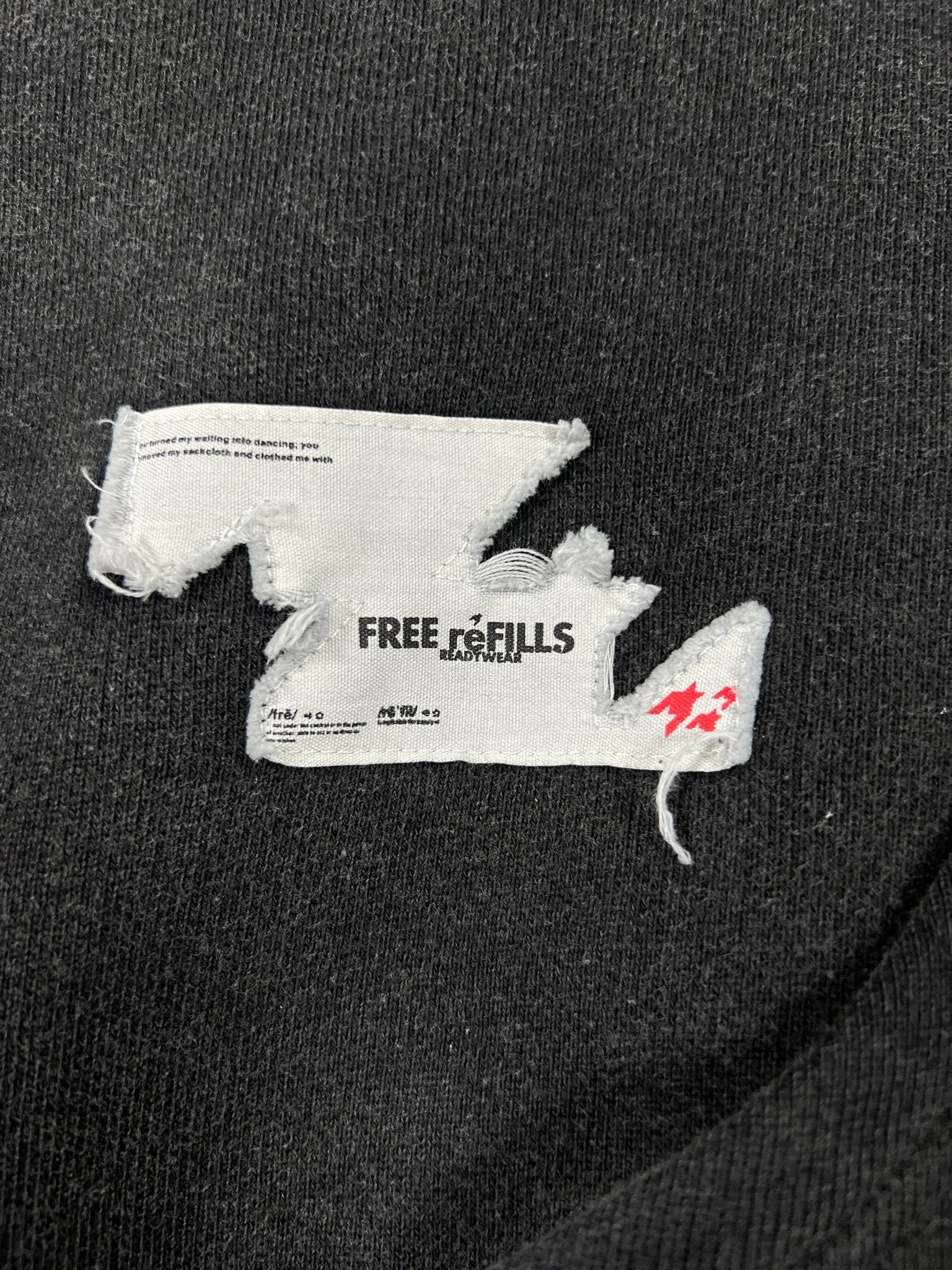 A torn white label with "FREE REFILLS" and faded black/red text is sewn onto the Free Refills Showcase Hoodie (FR-C3-27) in Vintage Black, complementing the hoodie’s distressed, vintage-washed appeal.