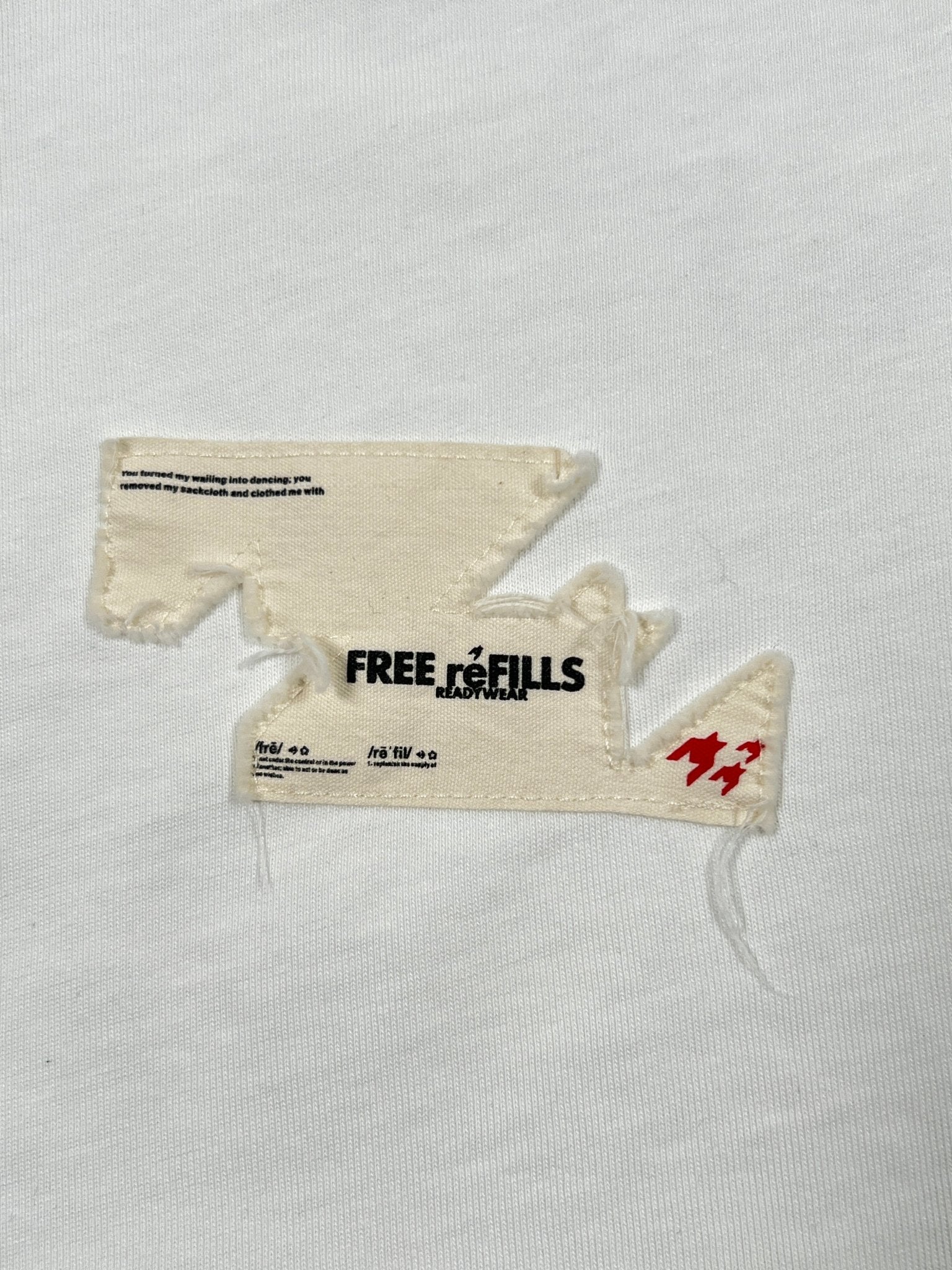 The FREE REFILLS Showcase Tee (FR-C3-7) in white features a jagged-edge fabric patch with "FREE REFILLS READYMADE" text and red accents for a bold, graphic look.