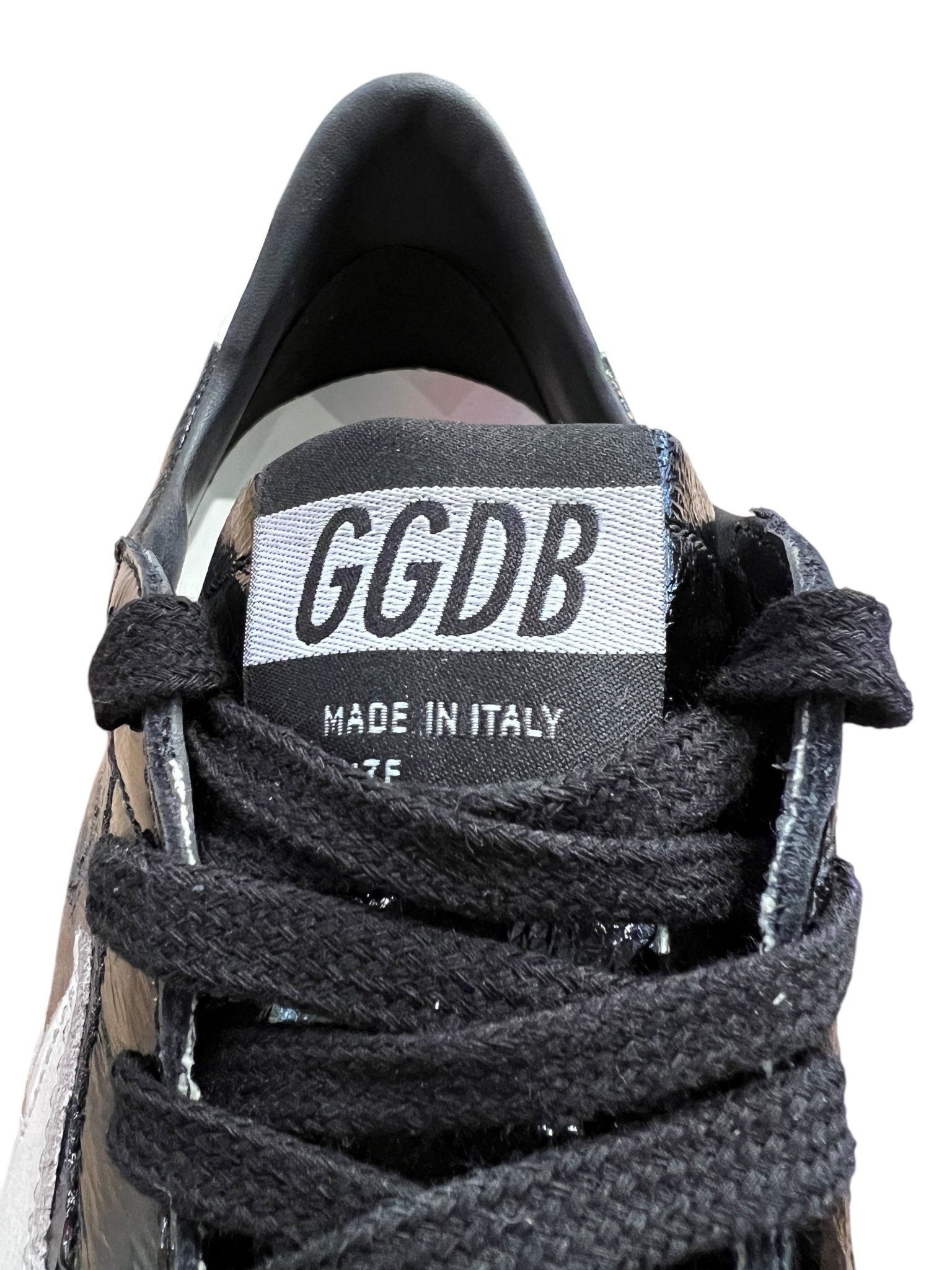 Close-up of a Golden Goose GMF00117 Ball Star sneaker tongue displaying "GGDB MADE IN ITALY," featuring black laces and various materials. The subtle distressed finish highlights the Italian craftsmanship of this Golden Goose product.