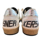 The Golden Goose GMF00117 Ball Star sneakers showcase metallic accents, a black leather star, and "SNER" on the left shoe with "KERS" on the right heel. Finished with a durable rubber sole, these stylish shoes are presented against a plain background. Brand: GOLDEN GOOSE.