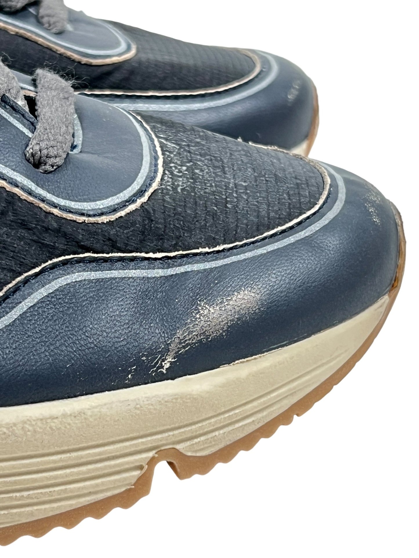 Close-up of the scuffed toe areas of two GOLDEN GOOSE GMF00126 RUNNING SOLE DK BLU/BLACK/SLV/WHT sneakers with gray laces and white rubber soles. The shoes show signs of wear and tear, embodying the rugged charm synonymous with GOLDEN GOOSE designs.