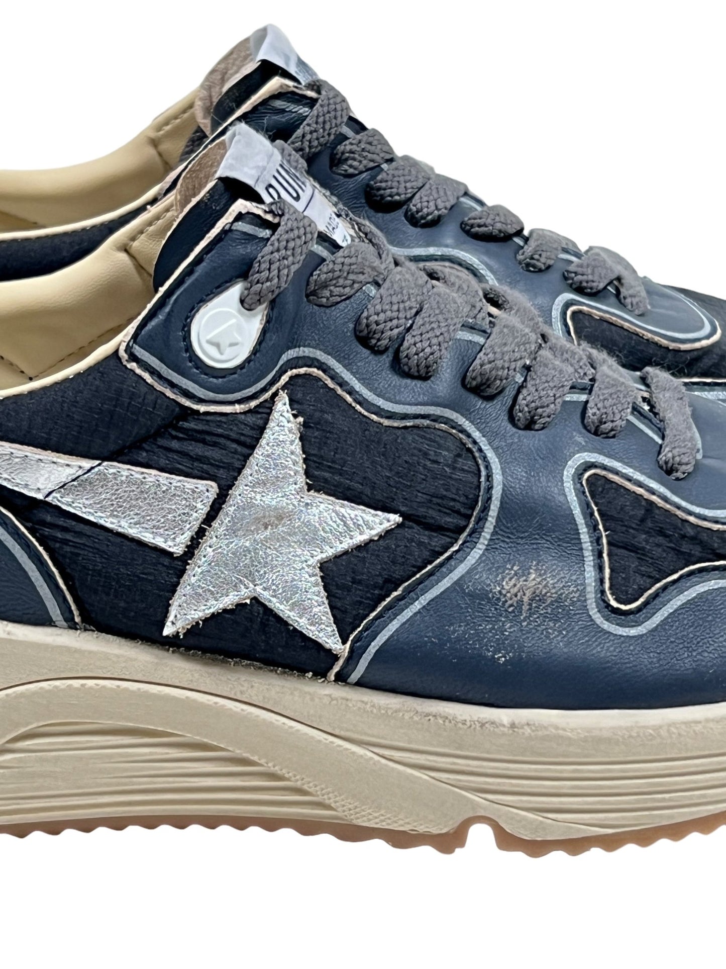 Close-up of the GOLDEN GOOSE GMF00126 RUNNING SOLE DK BLU/BLACK/SLV/WHT sneakers featuring white star accents and beige running soles. The dark blue shoes display signs of wear, with visible scuff marks on the sides.