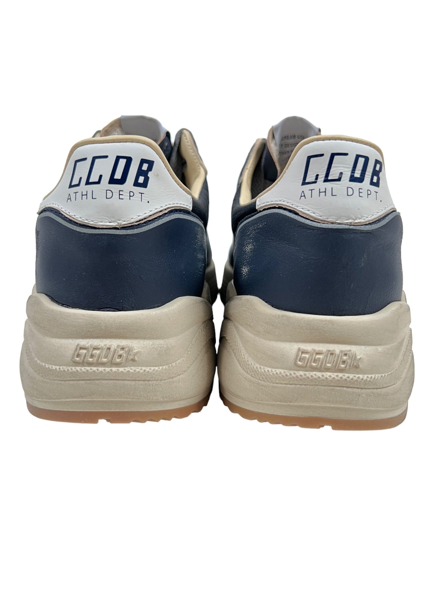 Back view of a pair of sneakers with "GCDB ATHL DEPT." written on the heel. These GOLDEN GOOSE GMF00126 RUNNING SOLE DK BLU/BLACK/SLV/WHT shoes feature a primarily dark blue and white design with beige soles.