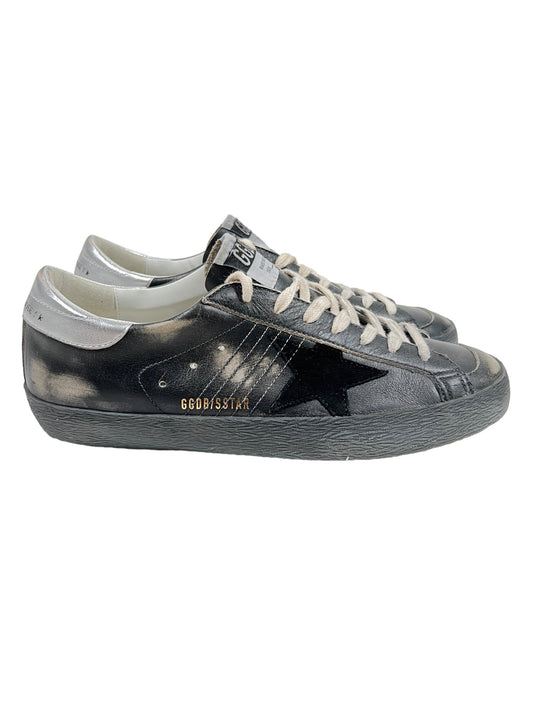 A pair of worn black and silver leather sneakers with white laces and a black star logo on the side. The shoes bear the brand name "GOLDEN GOOSE GMF00290 SUPER STAR LEATHER BLACK SILVER.