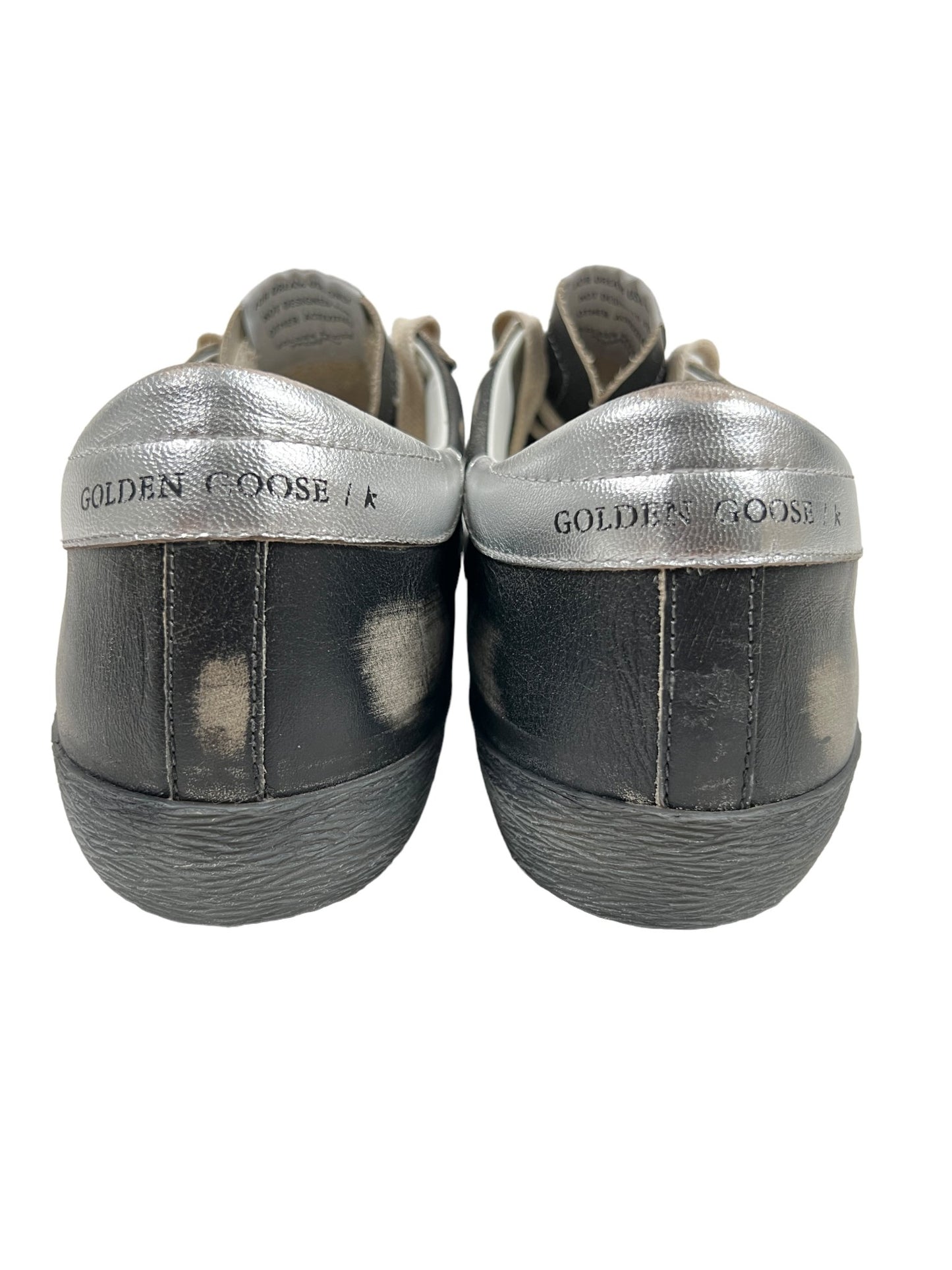 Back view of a pair of worn GOLDEN GOOSE GMF00290 SUPER STAR LEATHER BLACK SILVER sneakers featuring grey and black distressed details.