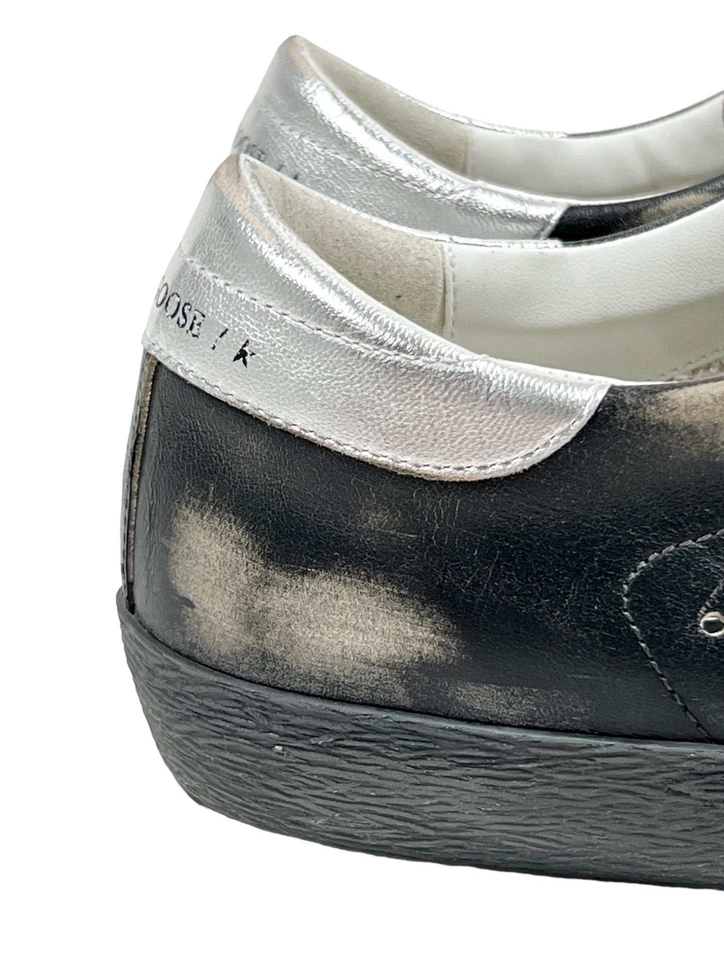 Close-up image of the GOLDEN GOOSE GMF00290 SUPER STAR LEATHER BLACK SILVER sneakers, highlighting worn-out and faded details on the back heel area.